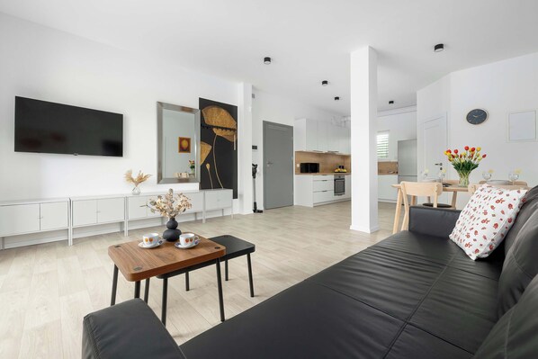 Ein modernes Wohnzimmer mit einer schwarzen Couch, einem Holztisch und einem Flachbildfernseher an der Wand.