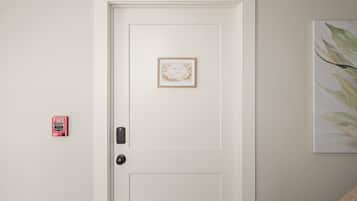 A white door with a framed picture, a fire alarm, and a wall-mounted artwork.
