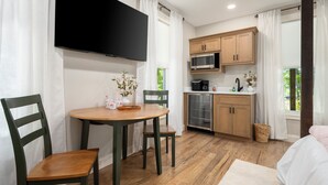 A modern kitchen with wooden cabinets, a microwave, and a dining area with a table and chairs. - Wild Rose Suite (Rome)