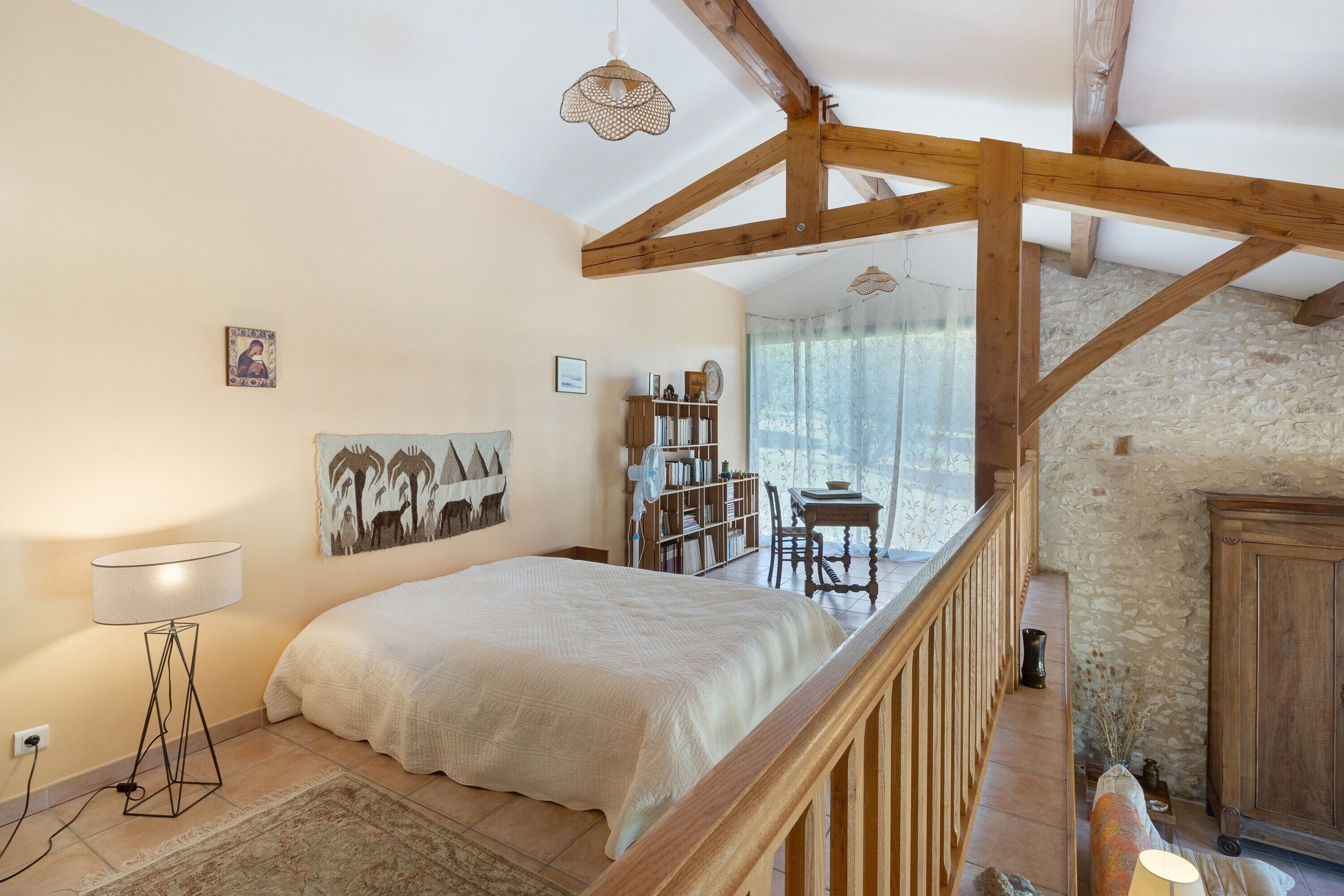 A bedroom with a bed, a standing lamp, a bookshelf, and a stone wall.
