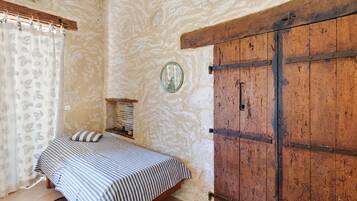 Ein Schlafzimmer mit einem Bett, einem Holzschrank, einem Spiegel und einem Fenster mit Vorhang.