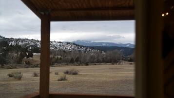 A view from a wooden-framed window overlooking a snowy landscape with trees and mountains.