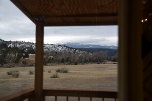 Une vue depuis une fenêtre à cadre en bois, donnant sur un paysage enneigé avec des arbres et des montagnes.