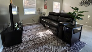 Ein Wohnzimmer mit einer schwarzen Ledersofa, einem Fernsehschrank, einem gemusterten Teppich und einer Topfpflanze.