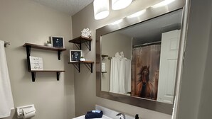 Ein Badezimmer mit einem großen Spiegel, einem Waschbecken und zwei Holzregalen mit gerahmten Bildern.