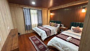A room with two beds, wooden flooring, a small table, and a window with curtains.