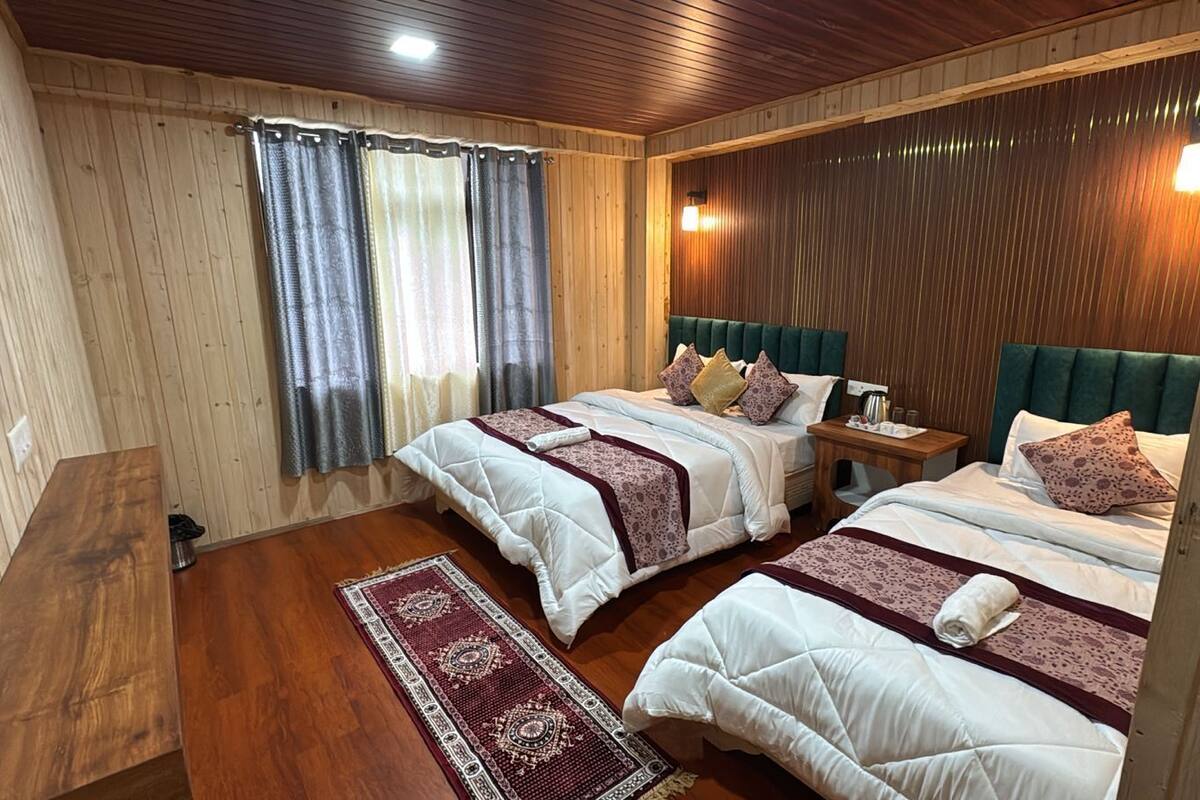 A room with two beds, wooden flooring, a small table, and a window with curtains.