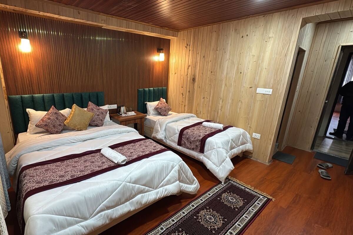 A room with two beds, wooden walls, a patterned rug, and a wooden ceiling.