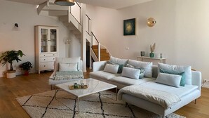 Un salon moderne avec un canapé blanc, une table basse, un escalier, un meuble et un tableau accroché au mur.