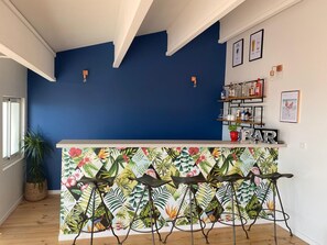 Eine Barbereich mit tropischem Wandpapier, hölzernen Barhocker und einer Flaschenregal.