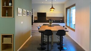 Une cuisine moderne avec une table en bois et des tabourets de bar, un luminaire suspendu et une grande fenêtre.