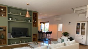 Un salon comprenant un canapé, un téléviseur, des étagères et un coin repas avec des chaises.