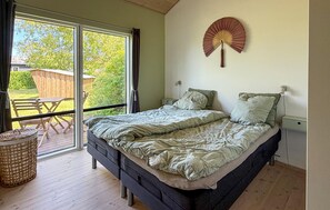 Ein Schlafzimmer mit Bett, Nachttisch, Lampe, Ventilator und Blick ins Freie.