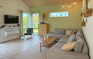 A living room with a sofa, a coffee table, a television, a cabinet, and a window with curtains. - Amazing home in Stege with sauna (Stege)