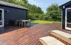Une terrasse avec une table et des chaises, un espace salon couvert et un bâtiment doté d’une porte et d’une fen être.
