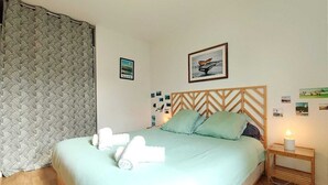 Un dormitorio con cama, almohadas, una mesita de noche y una pared decorada con cuadros.