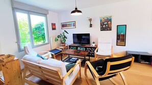 Una habitación con cama, una silla, televisor, una planta y obras de arte en las paredes.