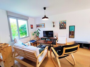 Ein Zimmer mit einem Bett, einem Sessel, einem Fernseher, einer Pflanze und Kunstwerken an den Wänden.