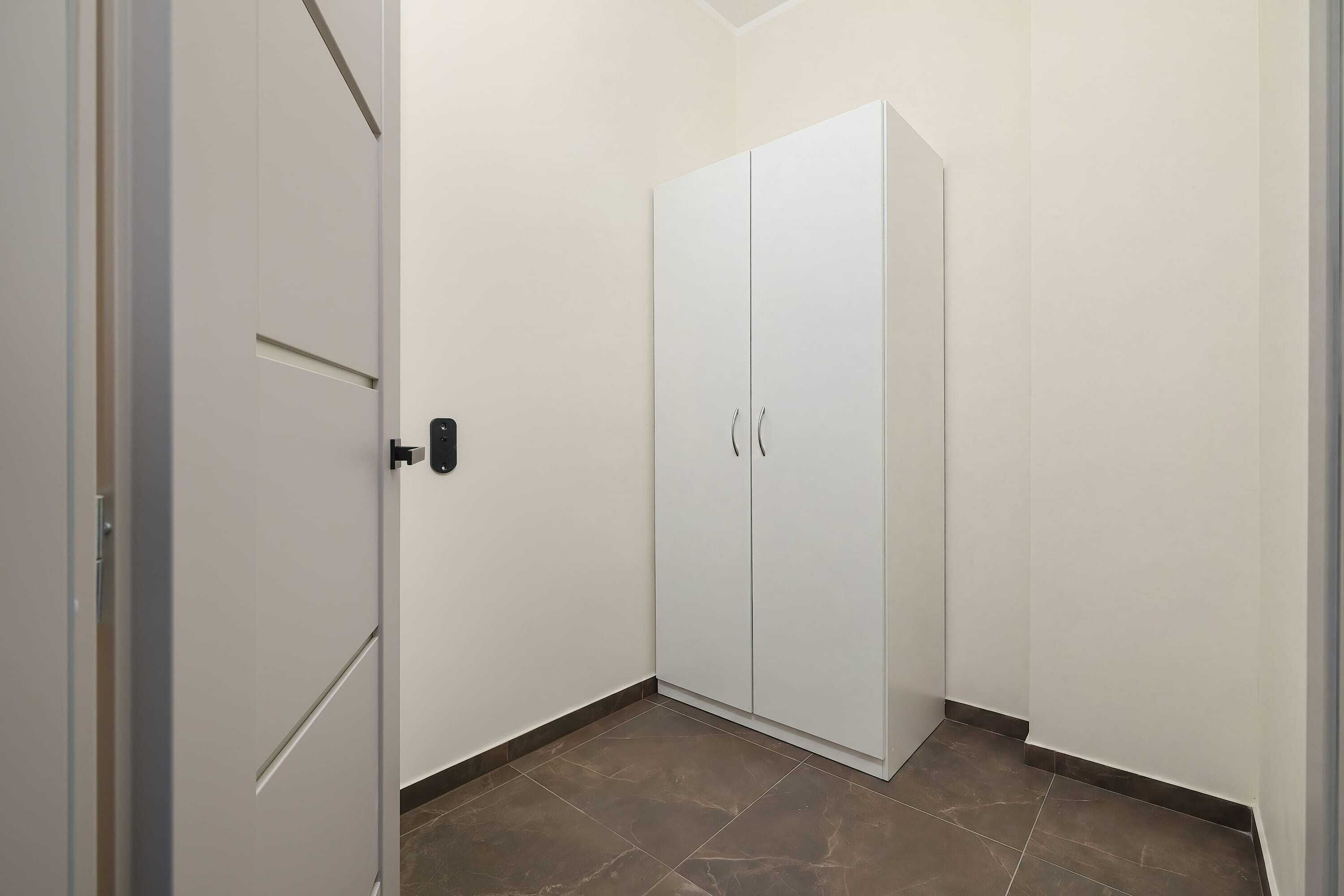 A room with a white wardrobe, a door, and a tiled floor.