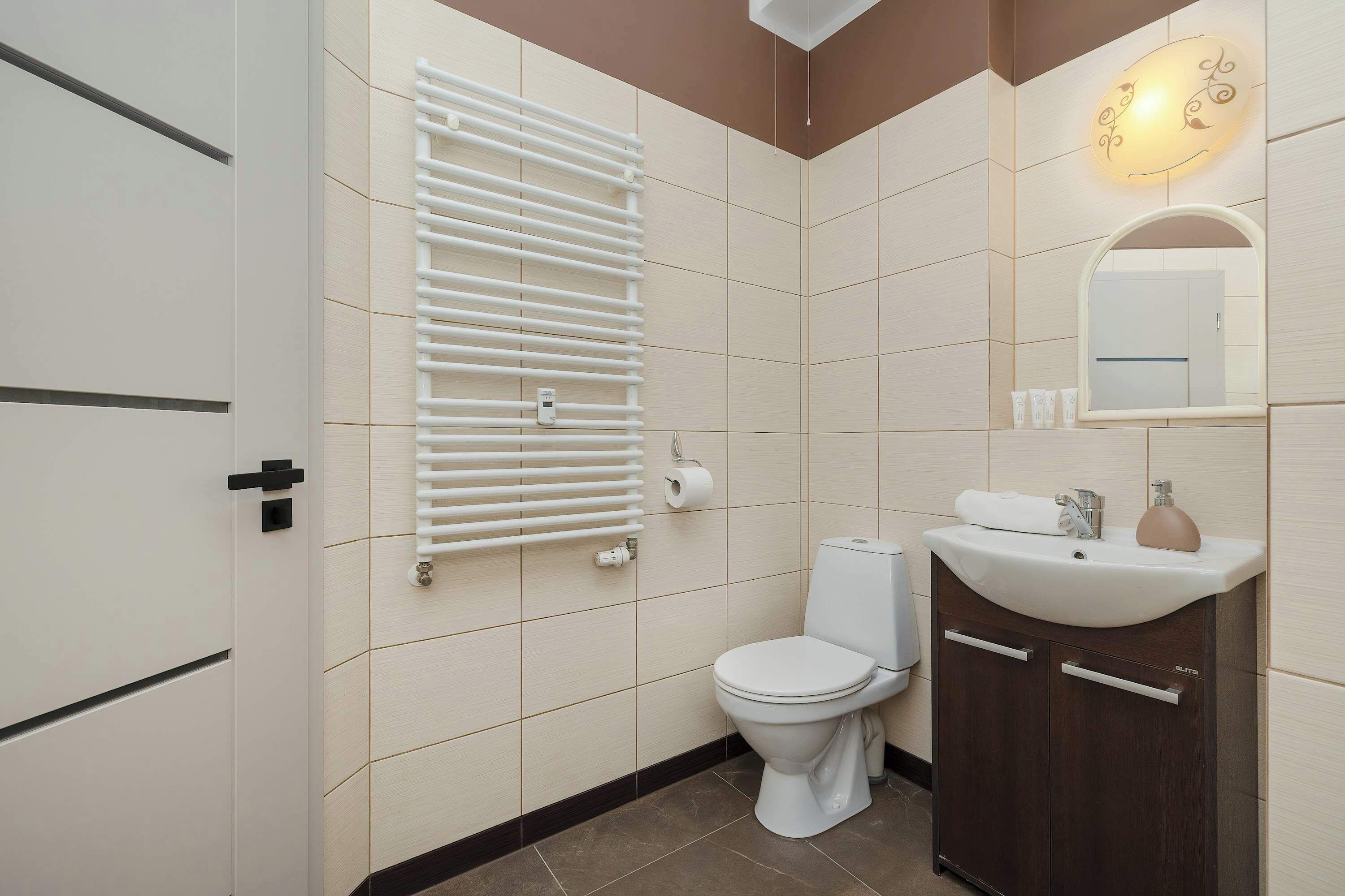 Ein Badezimmer mit Toilette, Waschbecken, Spiegel, Handtuchhalter und einer Wandleuchte.