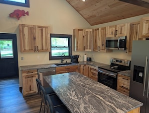 A modern kitchen with wooden cabinets, granite countertops, a stainless steel refrigerator, and a built-in oven. - Newly Remodeled Lakefront Cabin w/ Hot Tub & Private Dock (Merrifield)