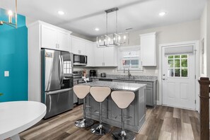 A modern kitchen with white cabinets, stainless steel appliances, a granite countertop, and a bar stool seating area. - Pier View-Sleeps 10-Pets-Walk to Beach (Myrtle Beach)