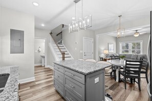 A modern kitchen with granite countertops, a central island, and a dining area with a round table and chairs. - Pier View-Sleeps 10-Pets-Walk to Beach (Myrtle Beach)