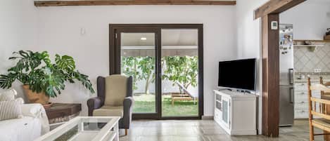 A living room with a sofa, armchair, coffee table, TV, and a kitchen area with a refrigerator.