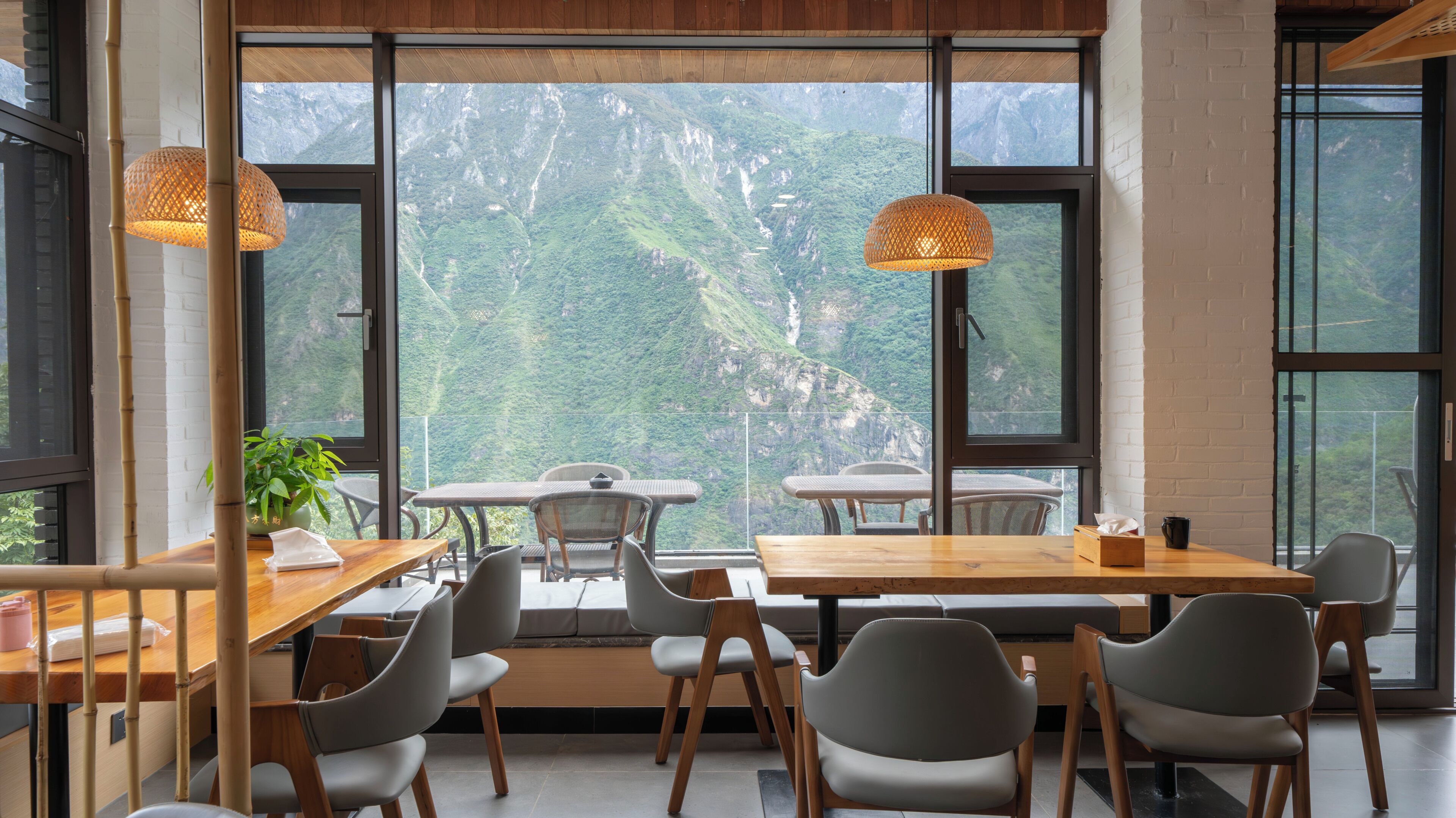 Un espace de restauration moderne doté de grandes fenêtres, de tables et de chaises en bois, offrant une vue sur un paysage montagneux.