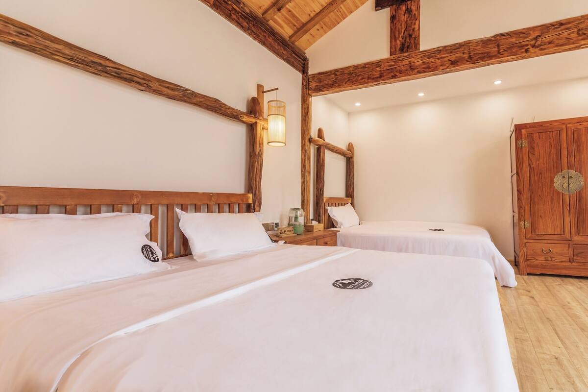 A hotel room with two beds, wooden beams, a wardrobe, and a mirror.