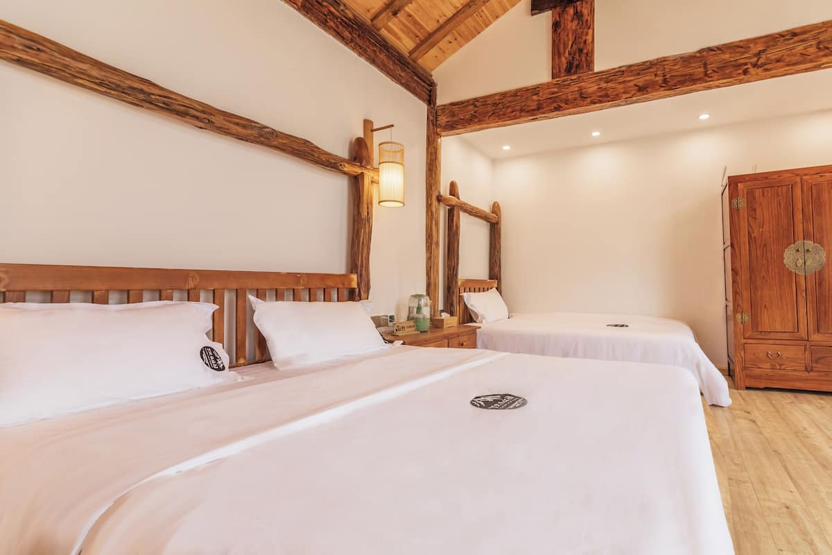 A hotel room with two beds, wooden beams, a wardrobe, and a mirror.