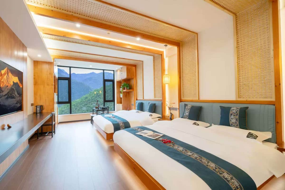 A hotel room with a large bed, a TV, a desk, and a view of mountains.