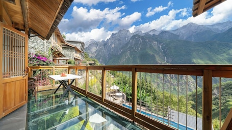 A glass-enclosed balcony with a table and chairs, overlooking a mountainous landscape.. Tiger Leaping Gorge yachajiao Manor