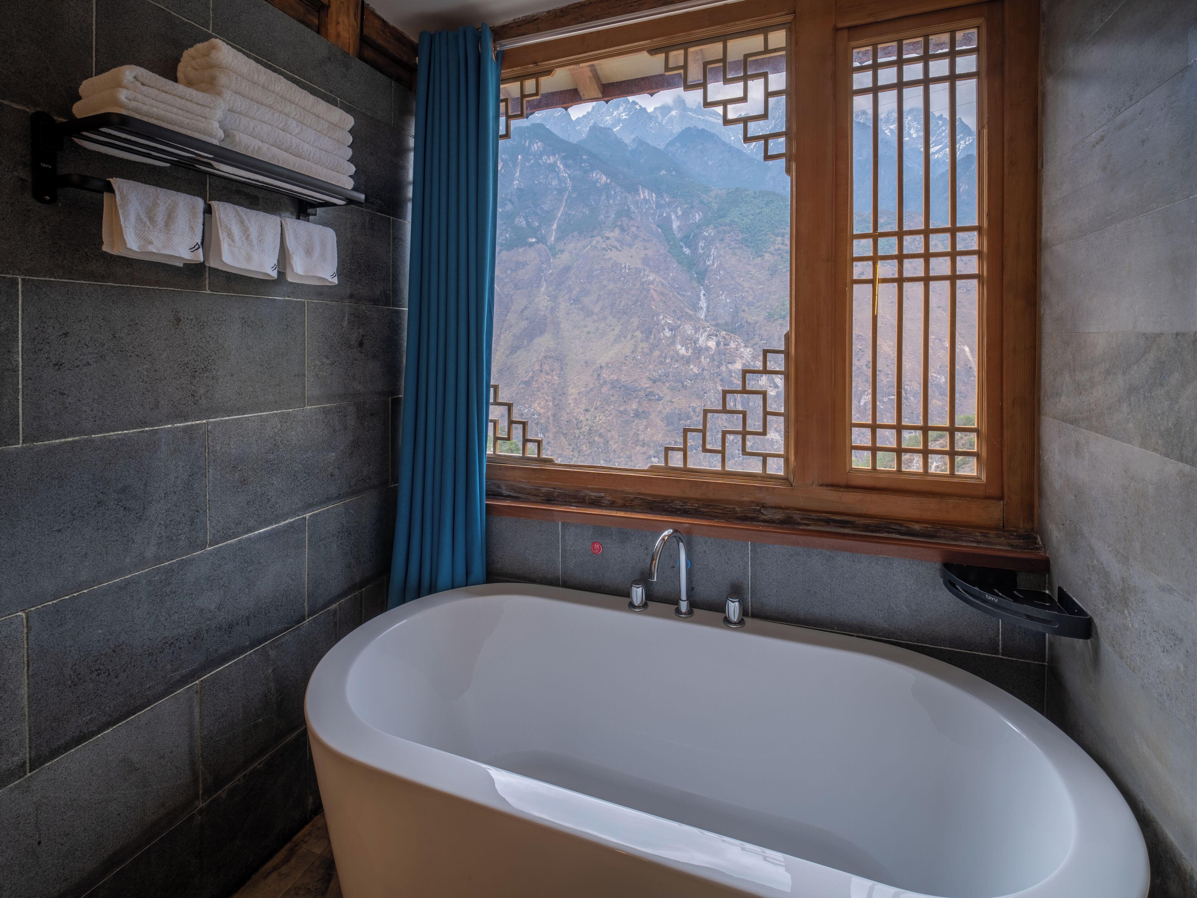 Un baño con bañera, una ventana con vistas a montañas y toallas en un perchero.