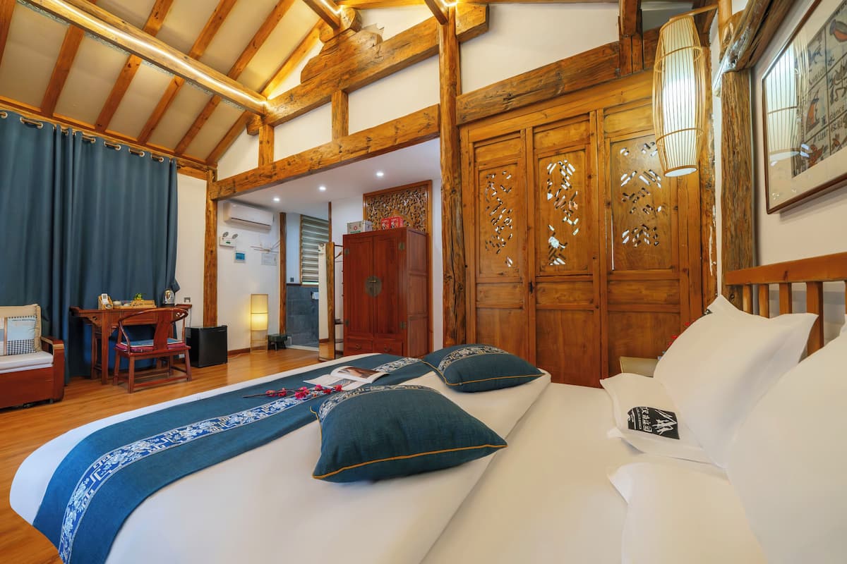 A bedroom with a wooden ceiling, a bed with blue and white bedding, a desk, and a wardrobe.