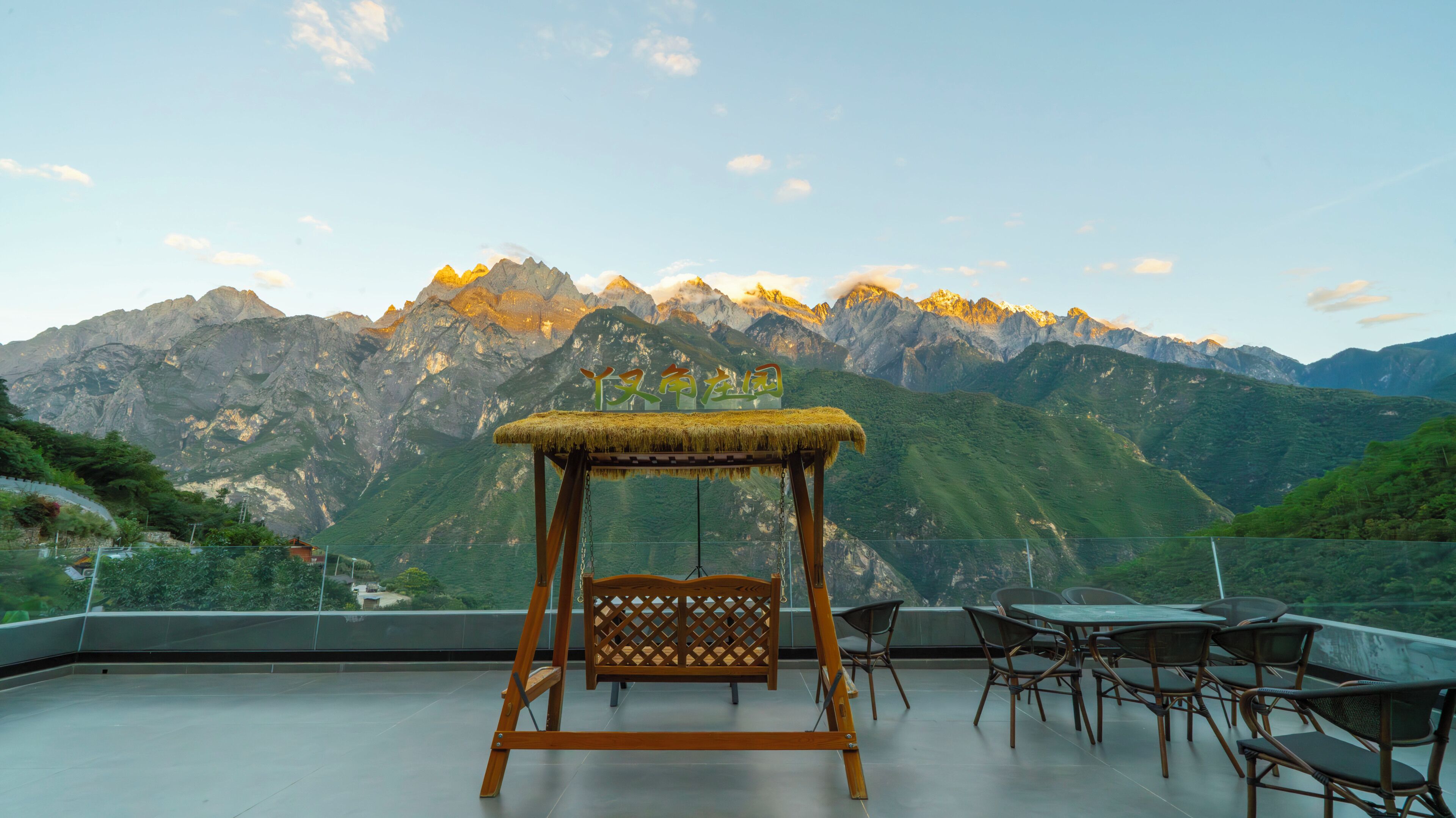 Una silla de madera con techo de paja, una mesa y sillas en una terraza con vista a la montaña.