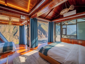 Une pièce avec un plafond en bois, un lit recouvert d’une courtepointe blanche et bleue, une fenêtre donnant sur les montagnes et un ventilateur de plafond.