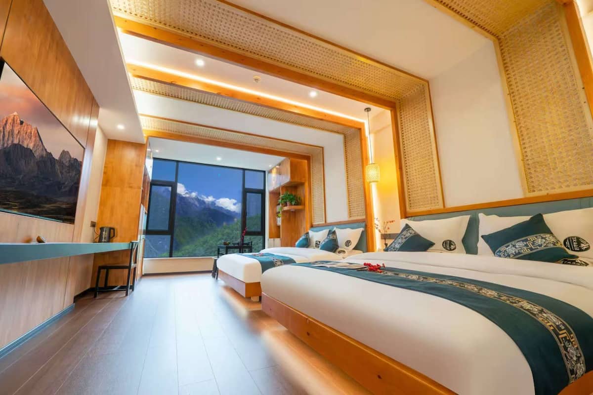 A modern hotel room with a large bed, a desk, and a view of mountains.