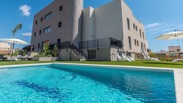 Un bâtiment moderne doté d’une piscine, de chaises longues et surplombant un ciel d’un bleu éclatant.