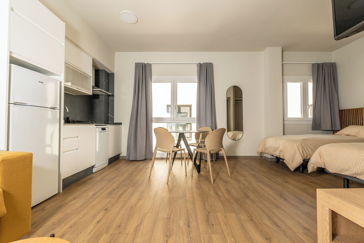 A modern room with a kitchen, dining area, and two beds.
