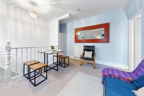 Ein Zimmer mit einer Treppe, einem runden Tisch mit zwei Hocker, einem Sessel, einer Couch und einem Spiegel an der Wand.