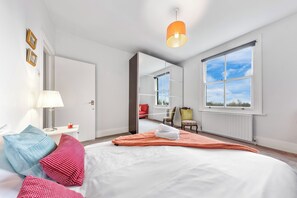 Ein Schlafzimmer mit Bett, Fenster, Spiegel, Lampe und Stuhl.