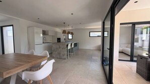 A modern kitchen with a central island, a dining area with a wooden table and white chairs, and a glass door leading to an outdoor seating area. - Beautiful 4-bedroom detached villa—with private pool and garage, fully equipped, near the ocean (Santa-Lucia-di-Moriani)