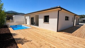 A modern house with a swimming pool, wooden deck, and a mountain in the background. - Beautiful 4-bedroom detached villa—with private pool and garage, fully equipped, near the ocean (Santa-Lucia-di-Moriani)