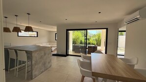 A modern kitchen with a dining area, a large sliding glass door to the outdoors, and a built-in air conditioning unit. - Beautiful 4-bedroom detached villa—with private pool and garage, fully equipped, near the ocean (Santa-Lucia-di-Moriani)