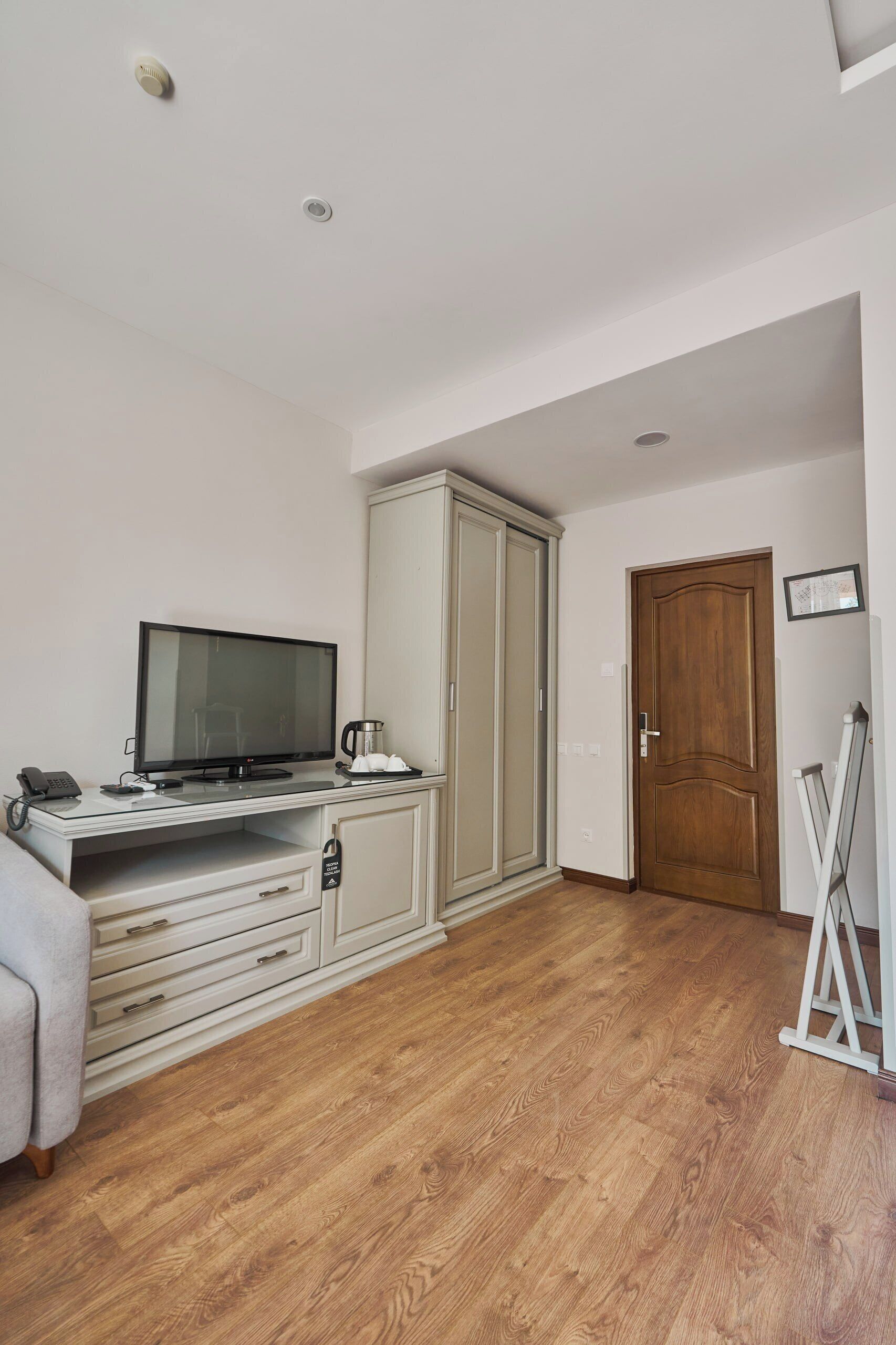 A room with a TV, a desk with a phone, a cabinet, a wardrobe, and a door.