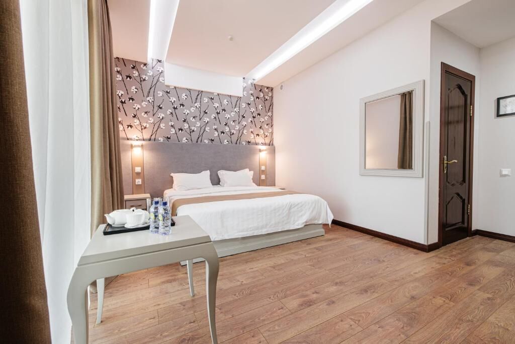 A hotel room with a bed, bedside table, and a wall with a floral pattern.
