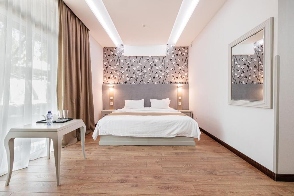 A hotel room with a bed, bedside tables, a desk, and a mirror.