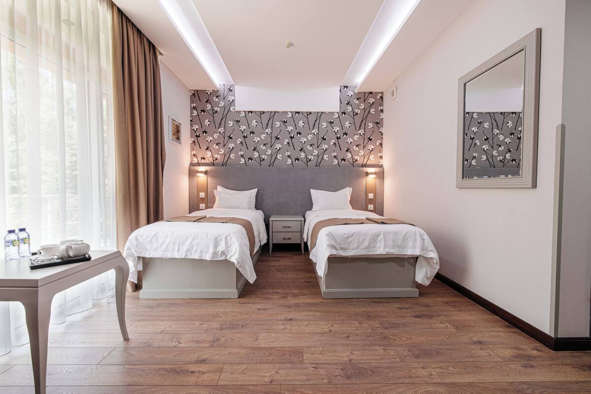 A hotel room with two beds, a bedside table, a mirror, and a floral wallpaper.
