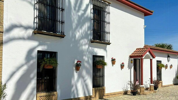 A white building with a red roof, multiple windows with black bars, and potted plants. - Private retreat with pool near Seville (Utrera)